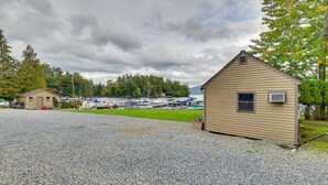 A gravel parking area with a small wooden building, boats docked in the background, and a lake. - Lake George Waterfront Cabin w/ On-Site Marina! (Bolton Landing)