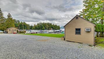 A gravel parking area with a small wooden building, boats docked in the background, and a lake.
