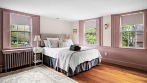 Ein Schlafzimmer mit Bett, Nachttisch, Lampe, Heizkörper und großen Fenstern.