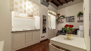 A kitchen with white cabinets, a wooden floor, a white table with a vase of red flowers, and a ceiling with exposed beams.