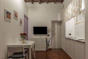 A small, compact kitchen with a dining area, a flat-screen TV, and a vase with flowers.