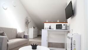 Una sala de estar moderna con un sofá, una mesa de centro blanca, una zona de cocina con electrodomésticos y un televisor montado.