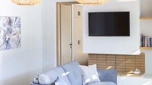 Una sala de estar moderna con un sofá gris, un televisor de pantalla plana montado en la pared y una estantería con libros.
