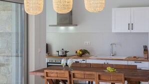 Una cocina moderna con una mesa de comedor de madera, lámparas colgantes de mimbre e incluso armarios blancos.