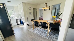 A modern kitchen with white cabinets, a black refrigerator, and a dining area with a wooden table and black chairs.