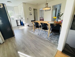 A modern kitchen with white cabinets, a black refrigerator, and a dining area with a wooden table and black chairs.
