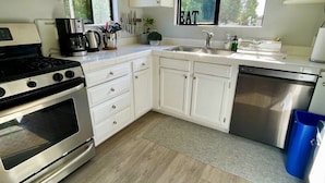 A modern kitchen with white cabinets, a stainless steel stove, a coffee maker, and a dishwasher.