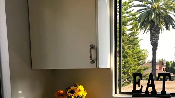 A kitchen with a window view of a palm tree and a sign that says "EAT".