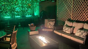An outdoor seating area with a fire feature, cushioned seating, and a green-lit backdrop.