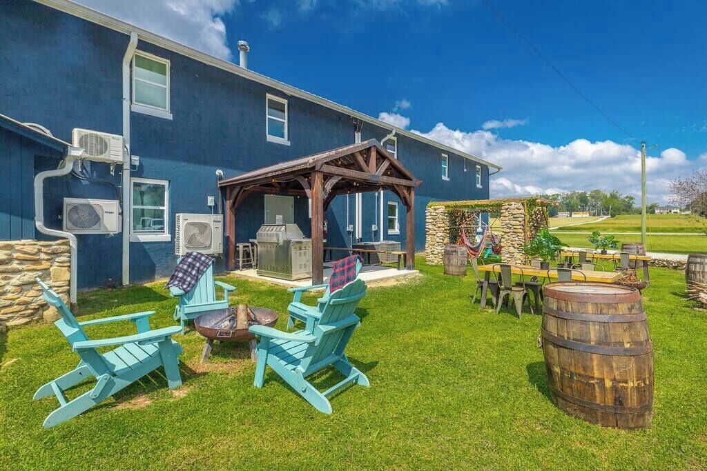 Una casa con un espacio exterior cubierto, una parrilla y mobiliario de jardín con sillas tipo Adirondack.