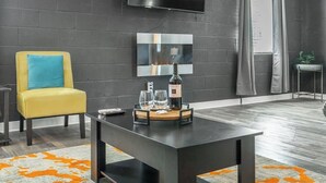 A modern living room with a black sofa, a yellow armchair, a coffee table with a bottle and glasses, a flat-screen TV, and a large mirror.