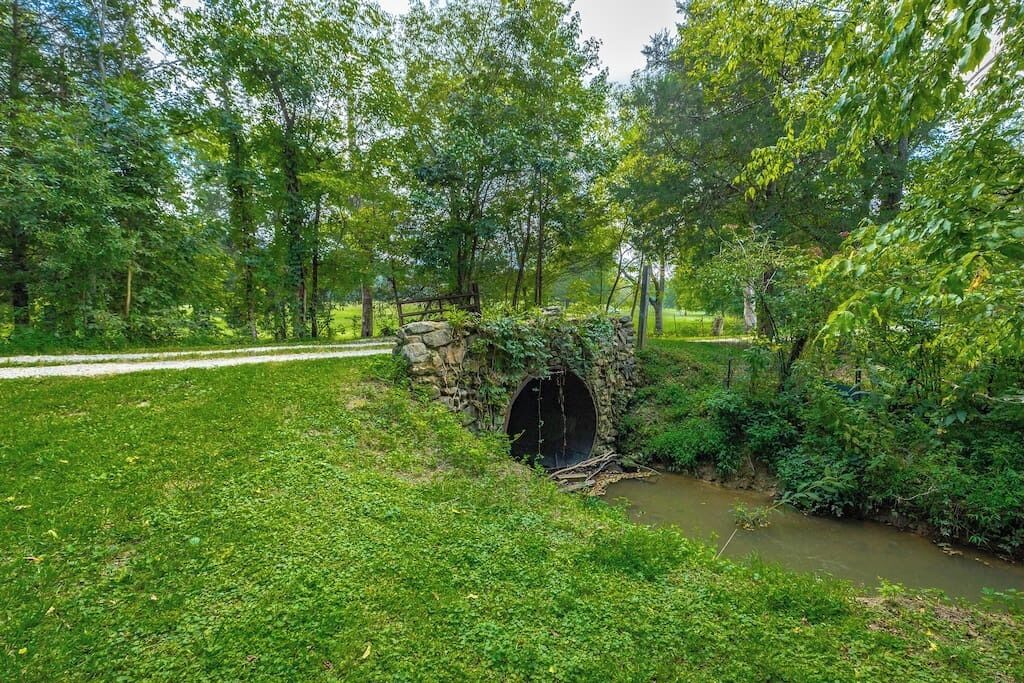 A stone bridge over a small stream in a park with lush greenery and trees.