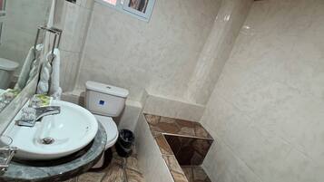 Un baño con lavamanos blanco, inodoro, zona de ducha y ventana.
