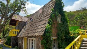 A stone house with a tiled roof, surrounded by greenery and a yellow staircase. - Refugio Cariguana  (El Valle de Anton)