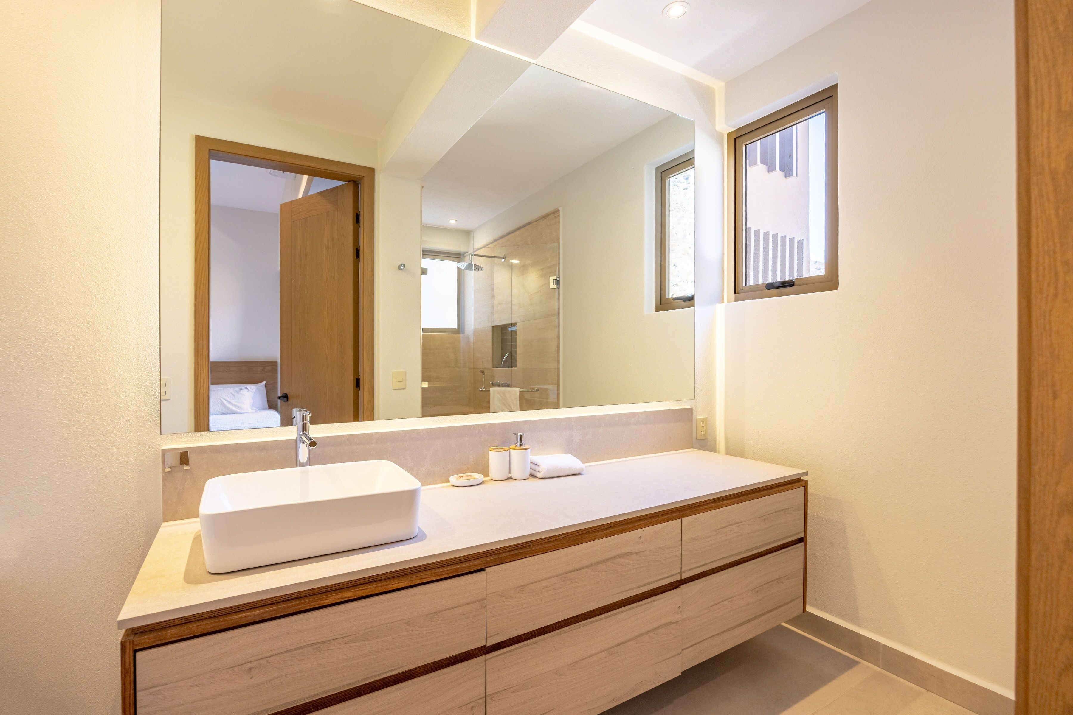 Une salle de bain moderne avec un grand miroir, un lavabo blanc et des meubles en bois.