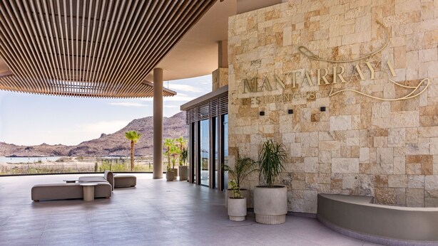 A modern hotel lobby with a stone wall, a reception desk, and a seating area with a view of the mountains.