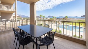 A balcony with a pool view, outdoor seating, and a clear sky.