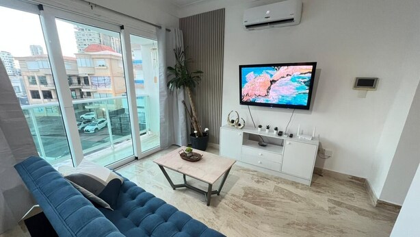 Un soggiorno moderno con un divano blu, un tavolino, una TV e una pianta.