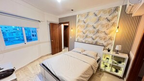 Una camera da letto moderna con un letto grande, un comodino con una lampada, una mensola a parete con piante e una finestra vista edifici.