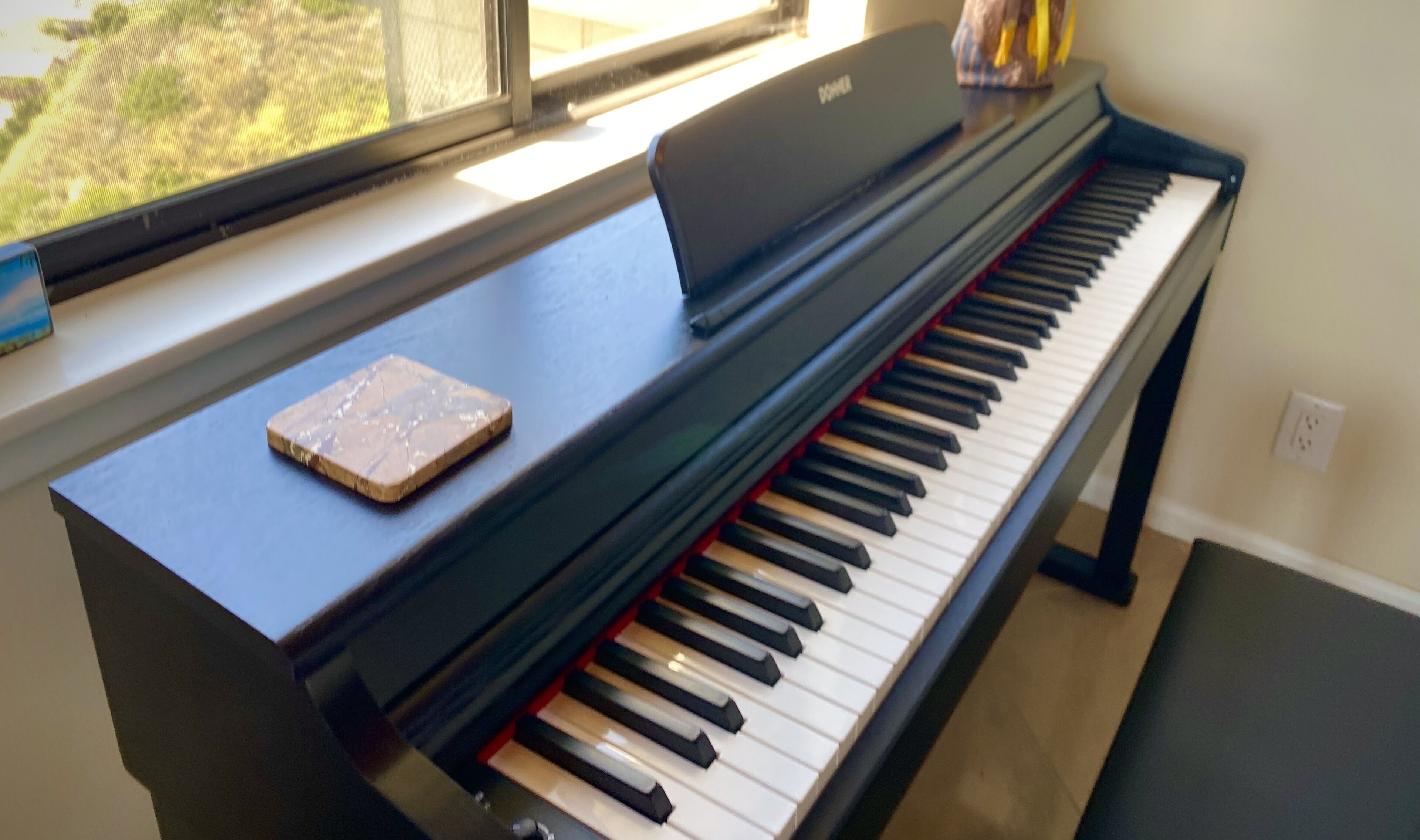Un piano con un libro de música encima, colocado cerca de una ventana.