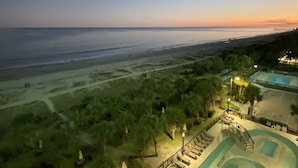 A resort with a pool, lounge chairs, and a view of the beach and ocean at sunset. - Direct oceanfront, separate bedroom, full kitchen - rates lower than last year ! (Myrtle Beach)