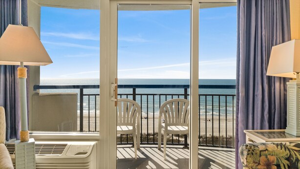 A balcony with two white chairs, a table, and a view of the ocean. - Direct oceanfront, separate bedroom, full kitchen - rates lower than last year ! (Myrtle Beach)
