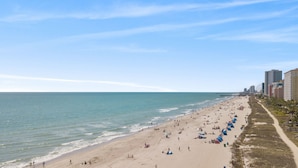 A wide beach with people and tents, a pier extending into the water, and tall buildings along the shore. - Direct oceanfront, separate bedroom, full kitchen - rates lower than last year ! (Myrtle Beach)