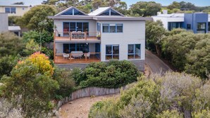 A modern two-story house with a balcony, surrounded by dense vegetation.