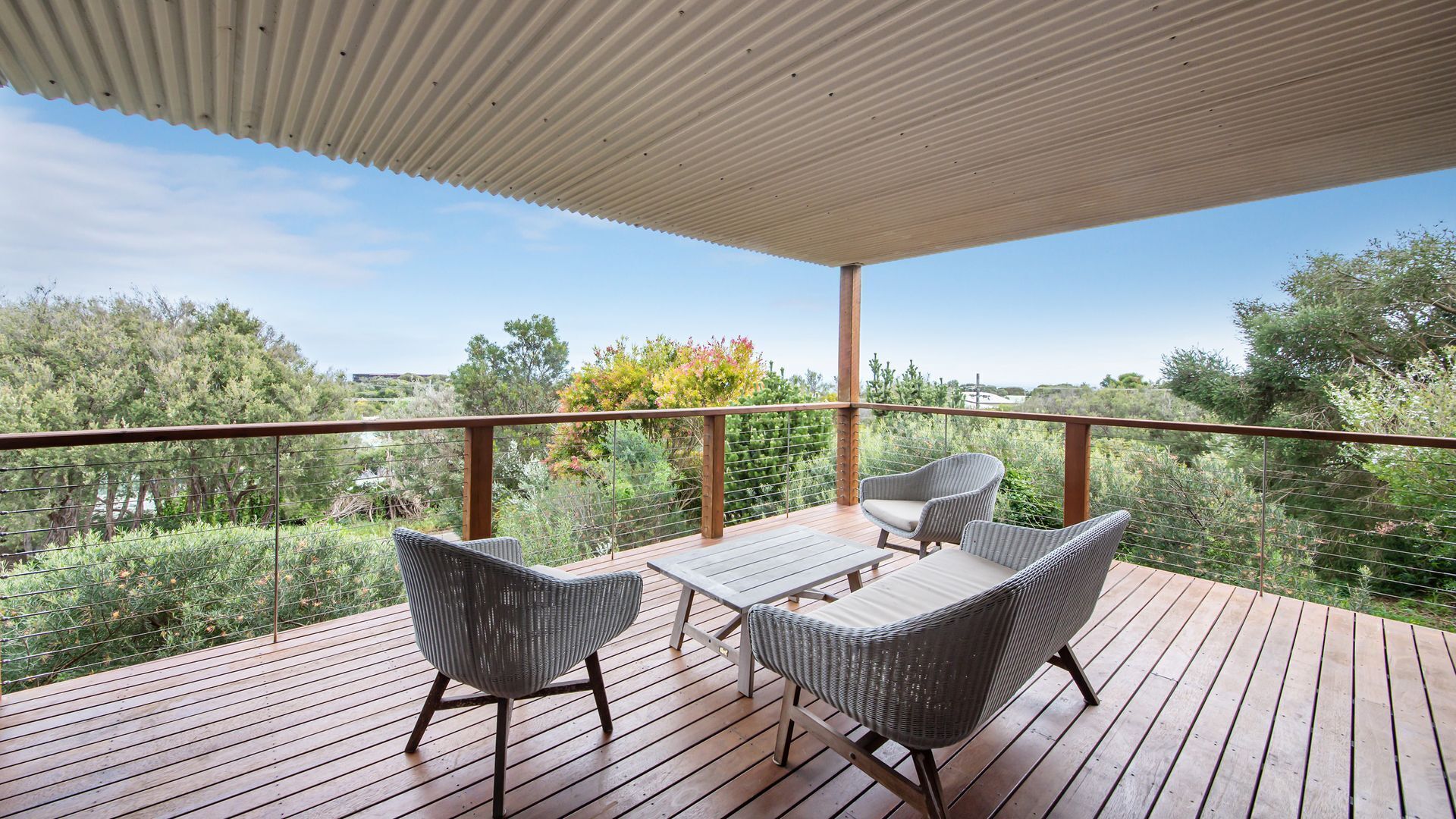 Une terrasse en bois, dotée de meubles en osier et d’une rambarde en métal, qui offre une vue sur un paysage naturel.