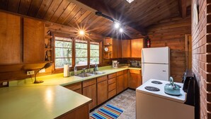 Une cuisine rustique dans un chalet, avec des murs en bois, une grande fenêtre, un évier, une cuisinière et un réfrigérateur.