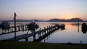 Un lago tranquilo al amanecer, con barcos amarrados a un muelle de madera.