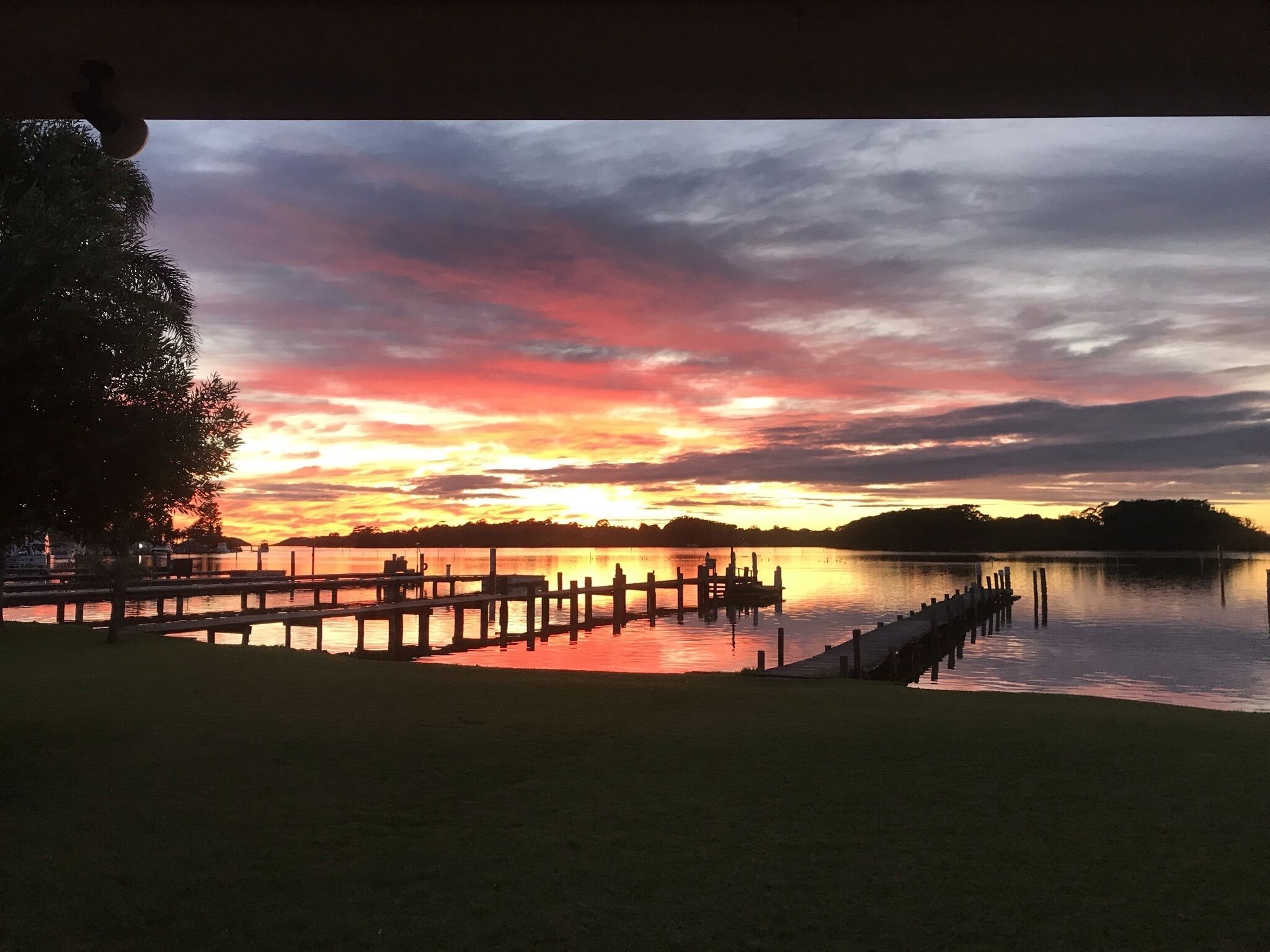 Une vue sur le lac, avec un quai s’avançant dans une eau calme, le tout entouré de prairies et d’arbres.