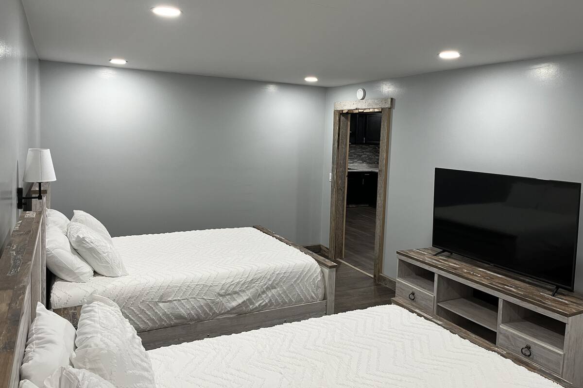 A modern hotel room with two beds, a TV, and a wooden entertainment unit.