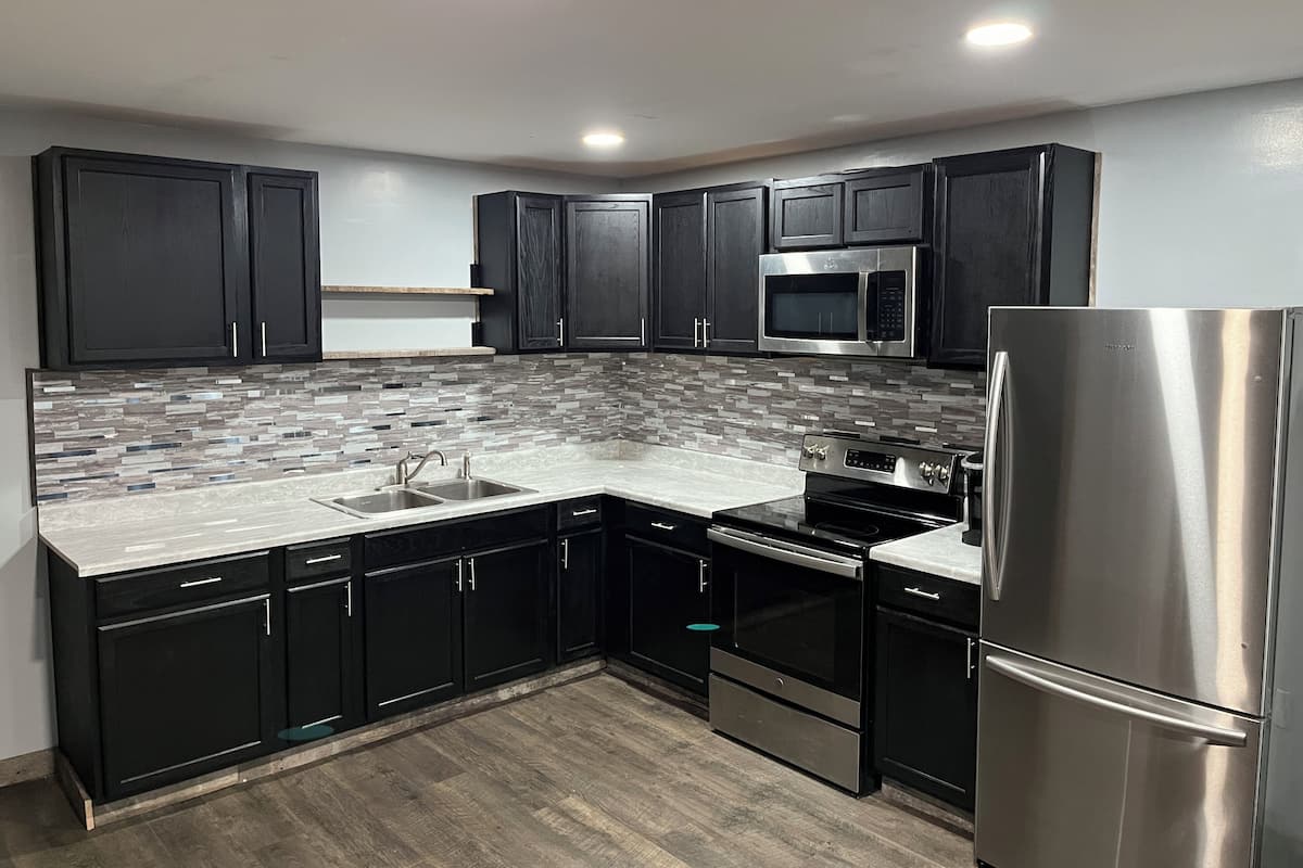 A modern kitchen with dark cabinets, a stainless steel refrigerator, a microwave, and a built-in oven.