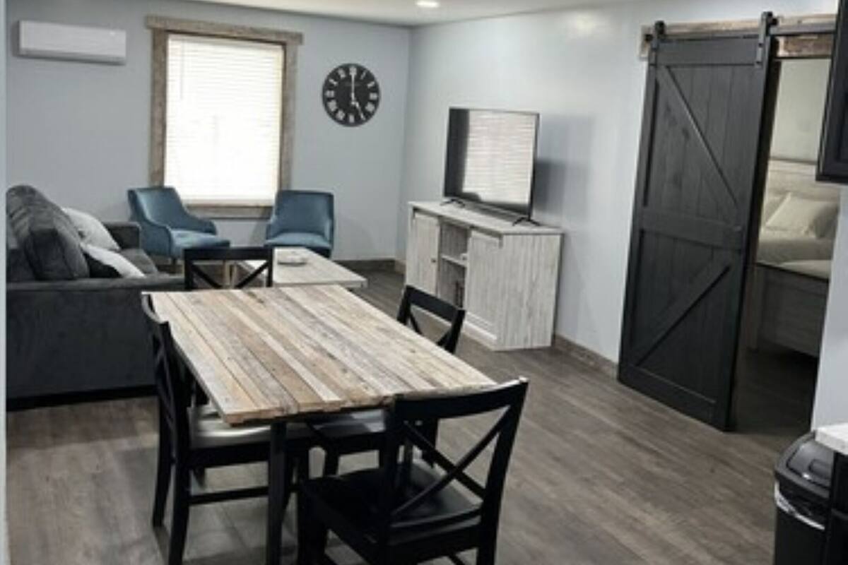A compact living space with a dining table, chairs, a sofa, a TV, and a sliding barn door.