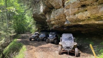 A dirt path with off-road vehicles parked under a rocky overhang.