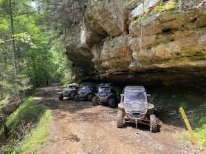 A dirt path with off-road vehicles parked under a rocky overhang.