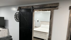 Ein Zimmer mit einer schwarzen Schiebetür, Holzboden, einem Bett mit weißer Bettwäsche, einem kleinen Tisch und einem Fernseher auf einem Schrank.