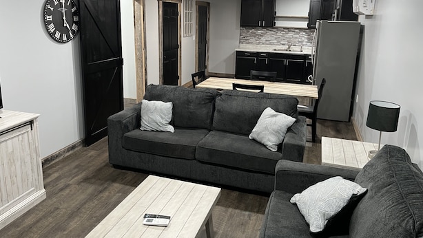 Ein kompakter Wohnbereich mit Sofa, Couchtisch, einer Uhr und einer Küchenzeile im Hintergrund.
