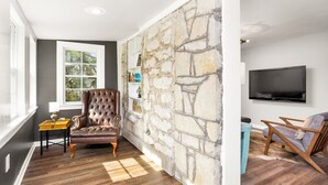 Una sala de estar con una pared de acento de piedra, un ventanal grande, un televisor de pantalla plana y dos sillones.