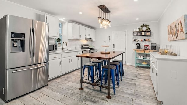 Una cocina moderna con electrodomésticos de acero inoxidable, una isla de madera con taburetes de bar, armarios blancos y una lámpara colgante.