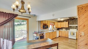 A kitchen with wooden cabinets, a stone accent wall, a built-in microwave, and a large wooden table. - Lead Hideaway w/ Fireplace, Grill & New Deck! (Lead)