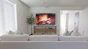 Ett vardagsrum med en platt-TV som är monterad på en träkonsol, en vit soffa och en krukväxt.