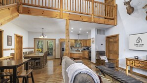 A spacious living area with a high wooden ceiling, a dining table, a sofa, and a kitchen in the background.