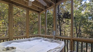 A hot tub with a wooden deck and large windows overlooking a forest.