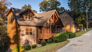 A log cabin with a stone foundation, a wooden deck, and a gravel driveway.
