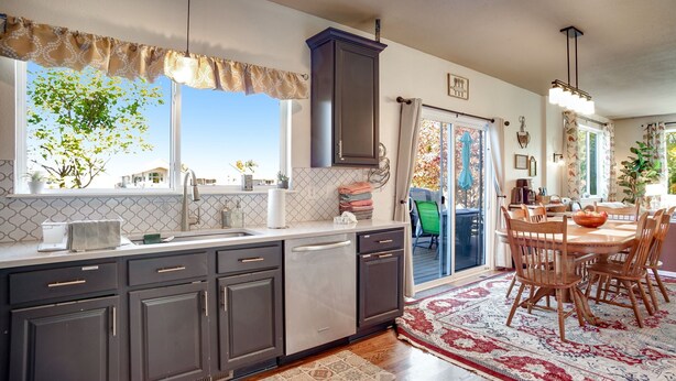 A modern kitchen with dark cabinets, a large window, and a dining area with a wooden table and chairs.