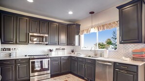 A modern kitchen with dark cabinets, stainless steel appliances, a patterned backsplash, and a wooden floor.