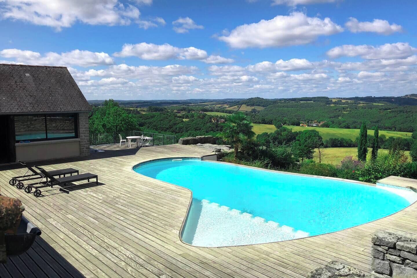 A swimming pool with a wooden deck, a lounge area, and a view of the countryside.