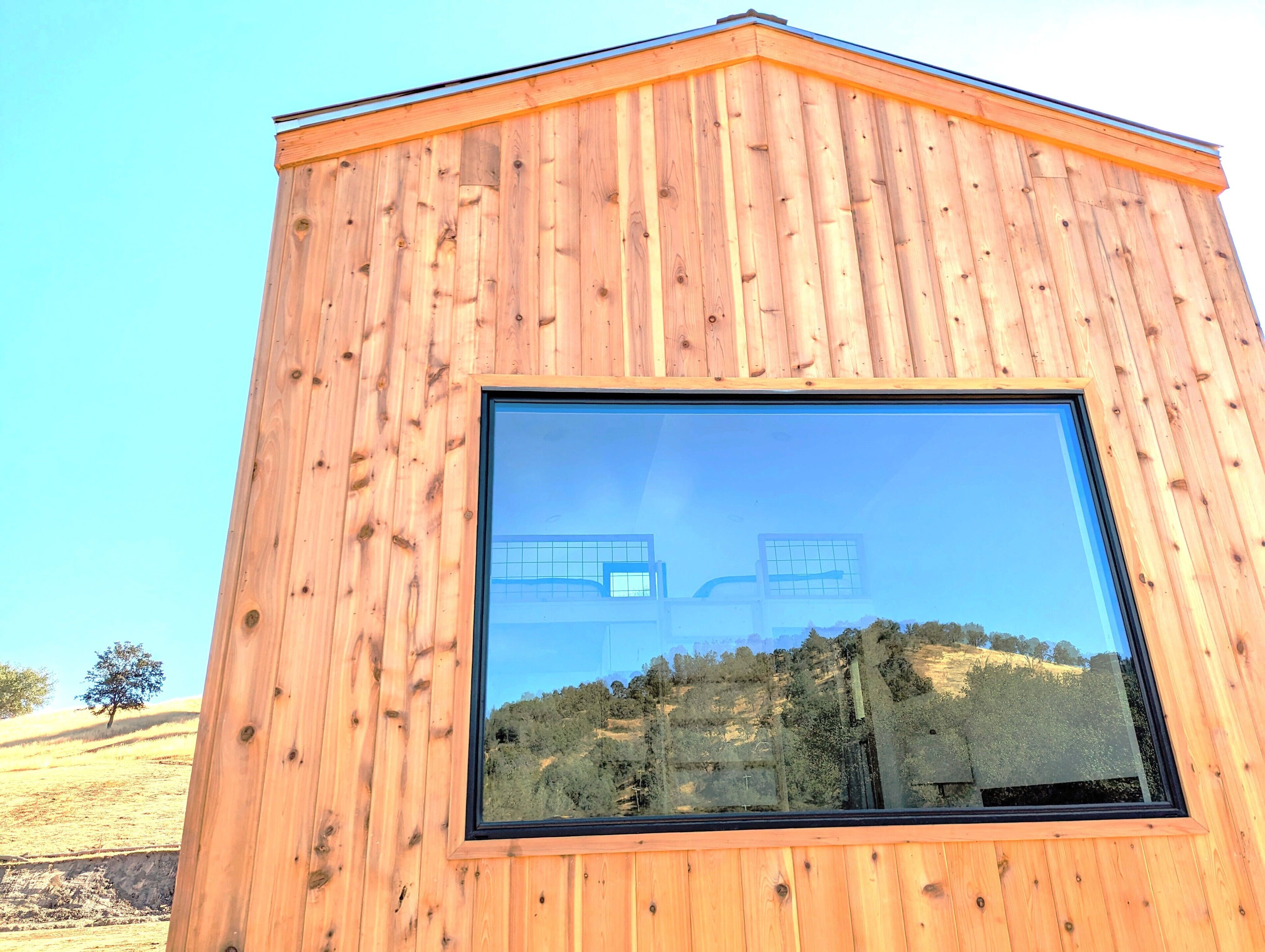 A wooden building with a large window reflecting a landscape.